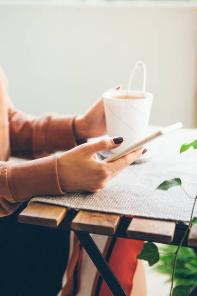 istock Woman standing at home during lock down. Drinking hot beverage - English breakfast tea while sitting and reading news from cellphone 1222217321