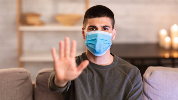 istock Serious guy in face mask gesturing stop sitting on couch 1222217564