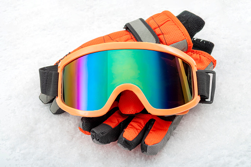 Snowboarding and skiing protective gear and winter extreme sports concept with ski goggles and cold weather gloves isolated on white snow background