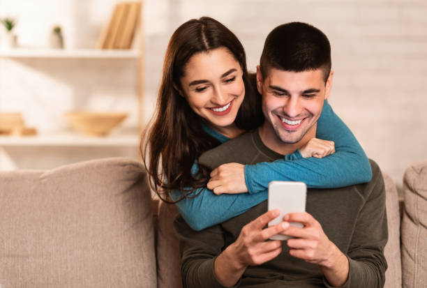 istock Lovely couple using cell phone sitting on sofa 1222228626