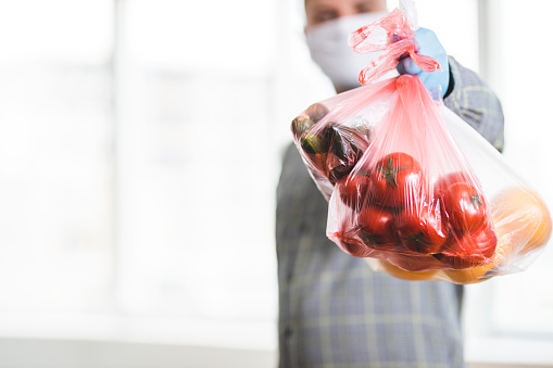 Unrecognizable delivery person holding plastic bag with fruit and vegetable