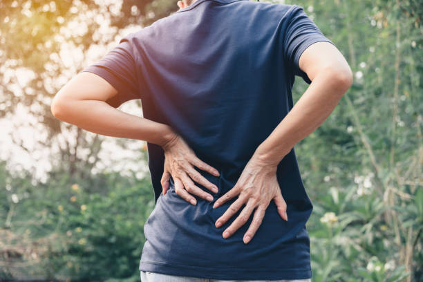 closeup hands of woman touching her back pain in healthy concept on nature background. - lower back pain imagens e fotografias de stock