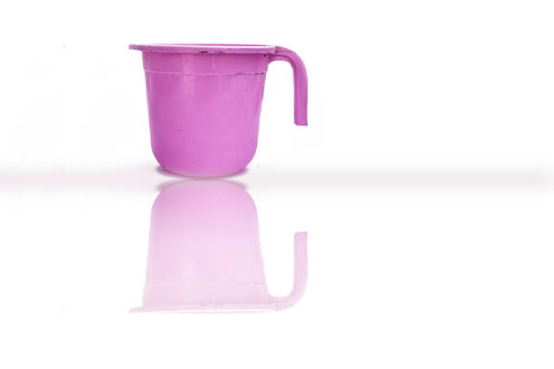 Pink colored plastic bathroom mug isolated on white-colored background white its glossy reflection.