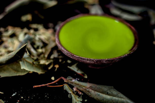 Close up shot of Banyan tree paste in a clay bowl on black glossy surface along with some dried leaf powder or Banyan tree leaves. Grind powder of Banyan tree leaf well mixed with water in a bowl. de cerca de la pasta de árbol banyan en un tazón de arcilla sobre la superficie brillante negro junto con un poco de hoja seca en polvo o hojas de árbol baniano. moler el polvo de la hoja del árbol baniano bien mezclado con agua en un tazón.