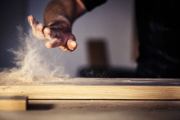 Carpenter brushes wood dust off table Dust is lit up in workshop carpenter stock pictures, royalty-free photos & images