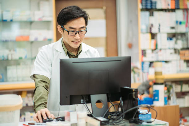istock Asian chinese smiling male pharmacist using computer key in data at pharmacy counter 1222233528