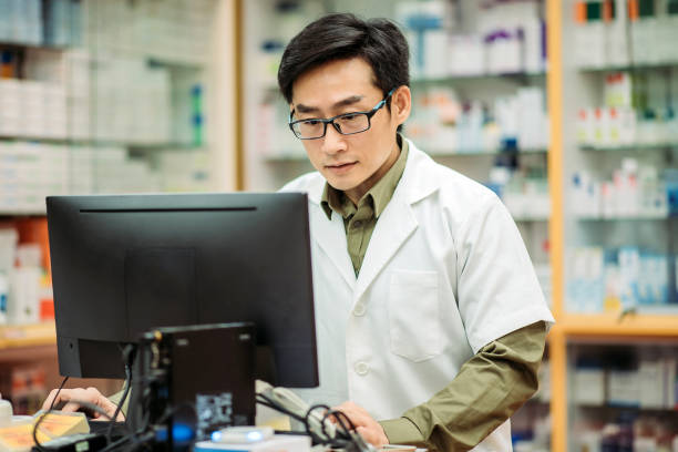 istock Asian chinese smiling male pharmacist using computer key in data at pharmacy counter 1222235619
