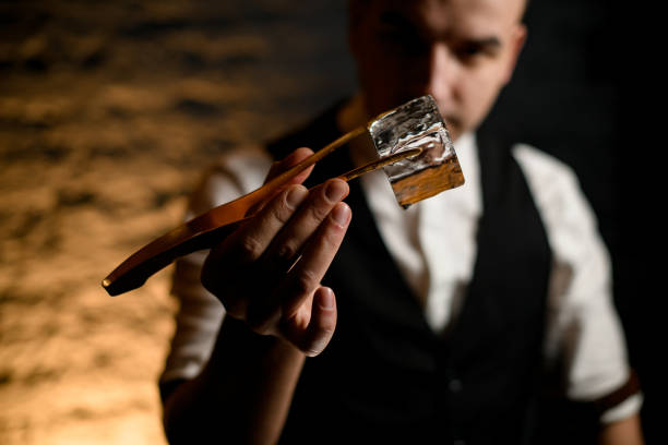 Close-up of cube of ice which young man holding using tweezers. Close-up cube of ice which young man at bar accurate holding with tweezers in his hand and look at it. giant cube stock pictures, royalty-free photos & images