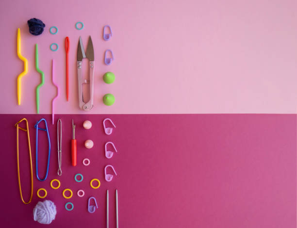 Top view or flat lay of colorful must-have plastic and aluminum knitting and crochet tools or accessories with threads on two-tone light and dark pink background,laid out symmetrically to the left. Copyspace on the right side, banner flatlay de coloridos imprescindibles herramientas de punto, ganchillo y costura o accesorios con hilos sobre fondo de dos tonos de color claro y rosa oscuro, dispuestos simétricamente a la izquierda. copyspace en el lado derecho. bandera