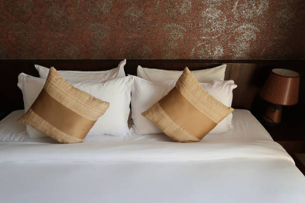 Image of luxury king size bed with gold scatter cushions and white pillows / folded sheets, wooden headboard against feature wall with golden pattern design