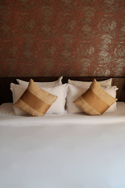 istock Image of luxury king size bed with gold scatter cushions and white pillows / folded sheets, wooden headboard against feature wall with golden pattern design 1222237265