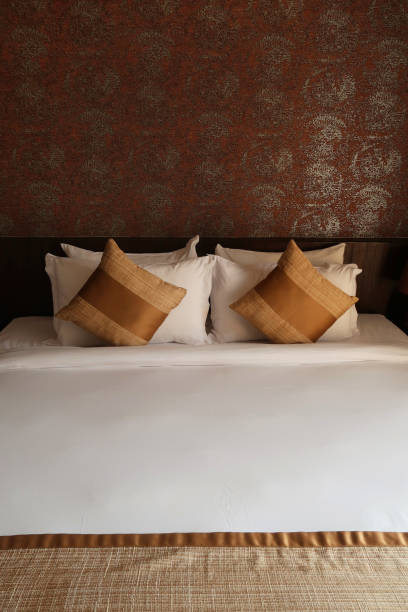 istock Image of luxury king size bed with gold scatter cushions and white pillows / folded sheets, wooden headboard against feature wall with golden pattern design 1222237753