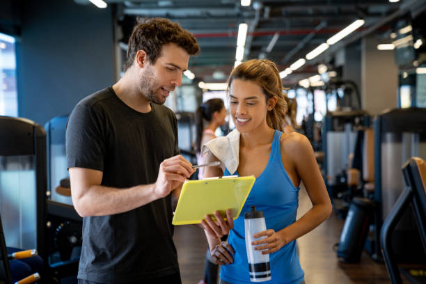 Personal trainer working at the gym and talking to a young woman Personal trainer working at the gym and talking to a young woman about her routine fitness instructor stock pictures, royalty-free photos & images