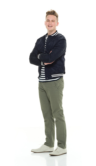 Full length of aged 18-19 years old caucasian male standing in front of white background wearing pants who is confident with arms crossed