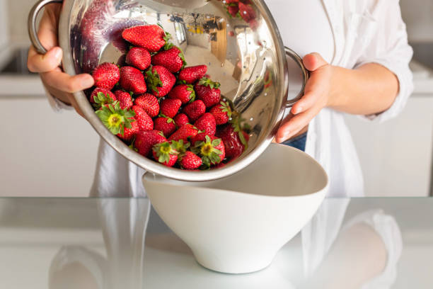 ステンレススチールザルのきれいな赤い熟したイチゴは、女性の手で水の下ですすがっています - washing fruit preparing food strawberry ストックフォトと画像