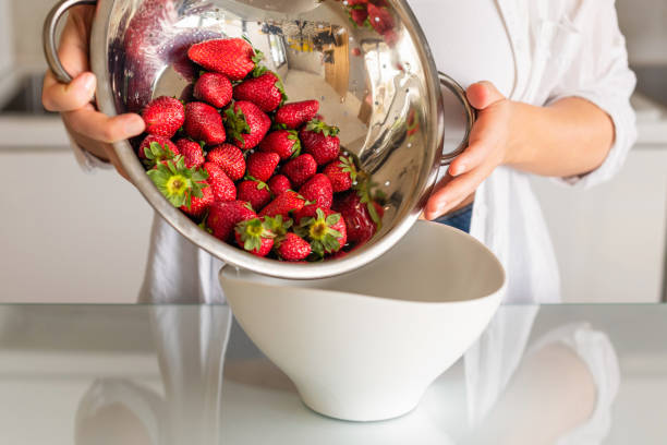 czyste czerwone dojrzałe truskawki w durszlak ze stali nierdzewnej są płukane pod wodą w kobiecej dłoni - washing fruit preparing food strawberry zdjęcia i obrazy z banku zdjęć