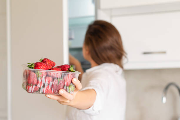 ein mädchen nimmt einen behälter mit frischen erdbeeren aus dem kühlschrank. rückansicht - washing fruit preparing food strawberry stock-fotos und bilder