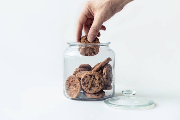 istock A hand taking cookies from a glass jar on white background. 1222243138