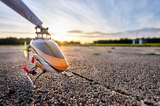 A RC helicopter standing on the ground in front of sunset sky on a beautiful summer day in a rural landscape. Seen in Germany in August.