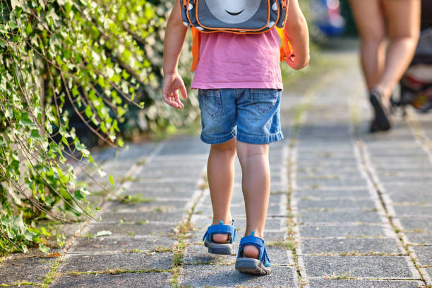 Rear view of 3 year old child walking behind its mother with rucksack stock photo