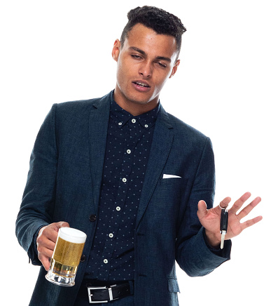 Portrait of with black hair african-american ethnicity young male businessman relaxing in front of white background wearing button down shirt who is drinking and showing hand raised who is drunk driving with arms raised and holding pint glass