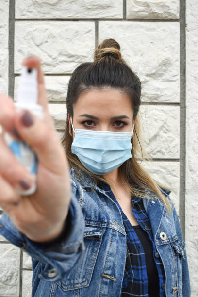 istock Woman outdoors with a face mask spraying hand sanitizer 1222247278