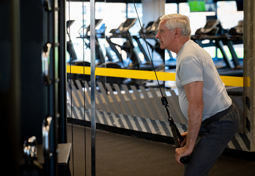 Latin American senior man exercising at the gym training his upper body using a machine - fitness concepts