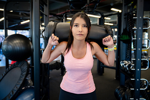 Portrait of a woman working out at the gym doing squats with a sand bag for extra weight â fitness concepts