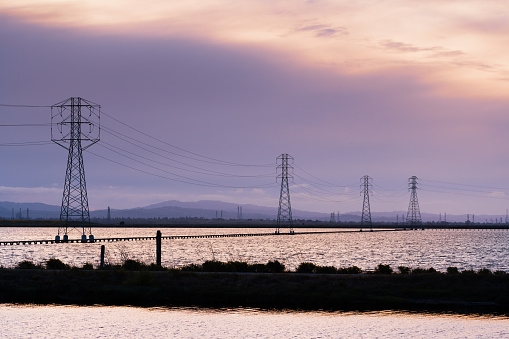 Sunset view of the tidal ponds of South San Francisco Bay Area with electricity towers crossing the wetlands; Mountain View, California