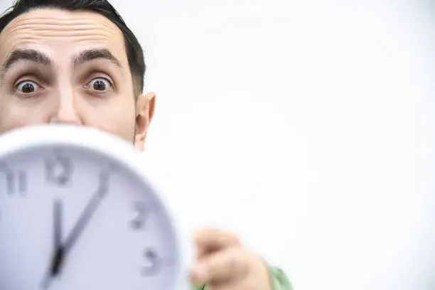 Cropped portrait of business man with shocked face expression, showing a clock, isolated on white background