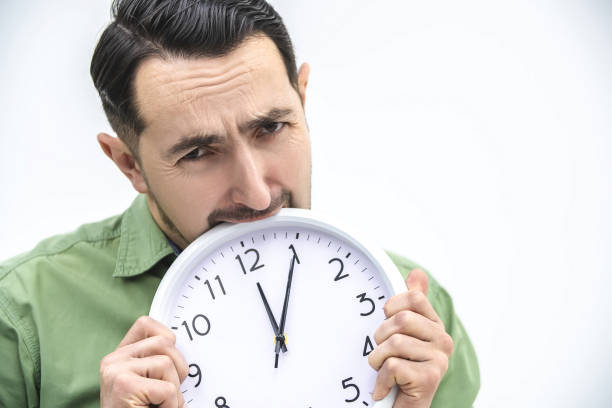 istock Totally exhausted man biting an alarm clock on a white background. 1222251175