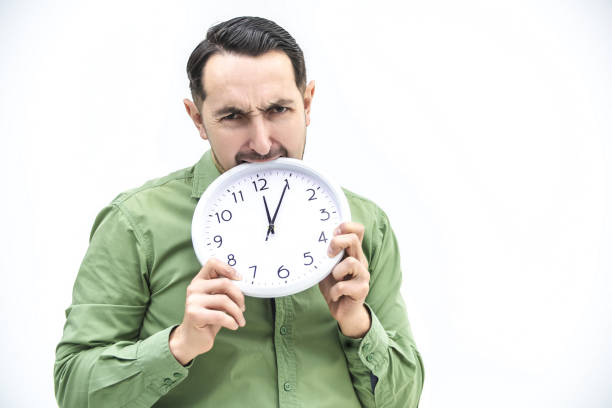 istock Totally exhausted man biting an alarm clock on a white background. 1222251205