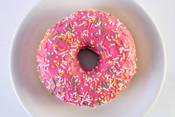 Pink frosted donut with colorful sprinkles on a white plate.