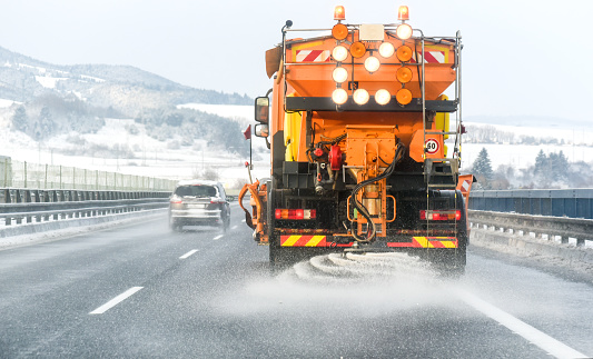 Snow plow on highway salting road. Orange truck deicing street. Maintenance winter vehicle.