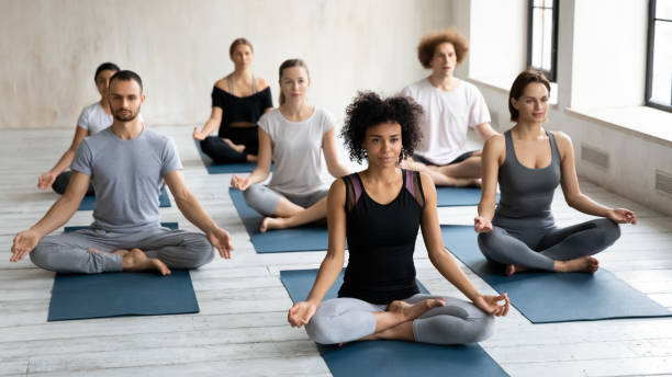diversos jovens sentados de pernas cruzadas praticando meditação juntos dentro de casa - men yoga meditating cross legged - fotografias e filmes do acervo