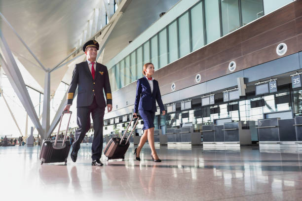 portrait of confident pilot with stewardess walking in airport - cabin crew pilot airport walking imagens e fotografias de stock