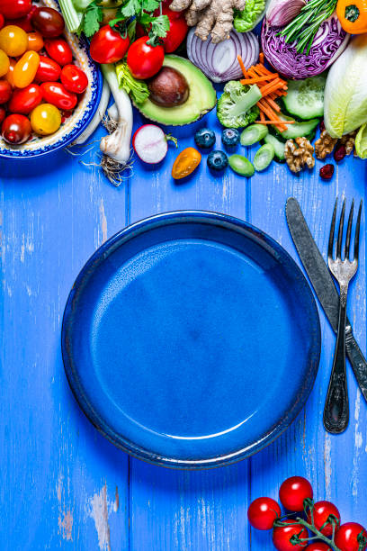 Vegan food: empty blue plate and healthy fresh vegetables border. Copy space