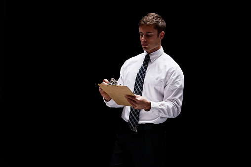 One person of aged 20-29 years old with short hair caucasian young male business person in front of black background wearing businesswear who is confident and holding clipboard