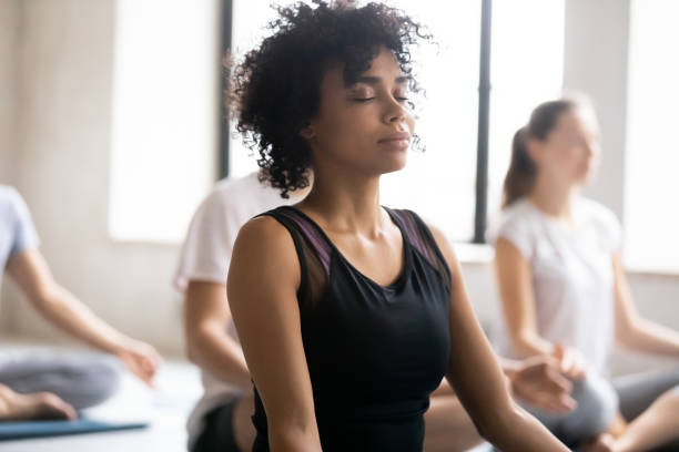 gli occhi chiusi femminili africani fanno pratica di meditazione con i soci - yoga class instructor yoga exercising foto e immagini stock