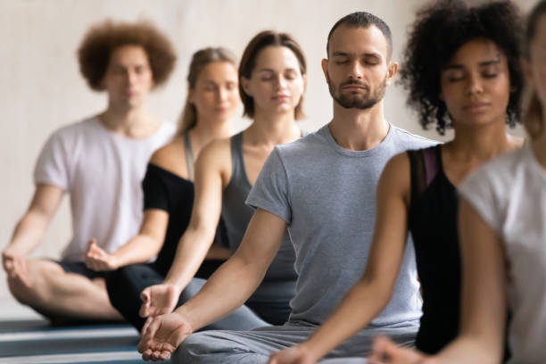 Group of diverse people meditating visualizing during yoga session Group of diverse people meditating together visualizing during yoga morning session, focus on Caucasian man seated cross-legged in row with associates, no stress, spiritual practise, lifestyle concept meditating stock pictures, royalty-free photos & images