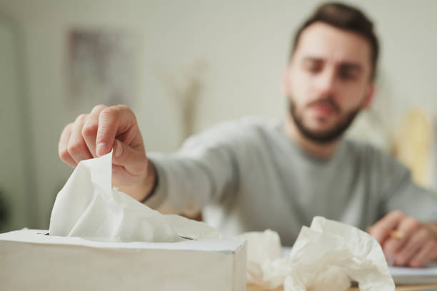 hand of sick businessman taking paper tissue from box while sitting by table - tissue box flu virus kleenex imagens e fotografias de stock