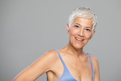 Portrait of beautiful mature woman with grey hair looking at camera. Attractive middle aged woman with beautiful smile isolated over grey background.