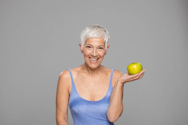 istock Happy senior woman with  apple against grey background. 1222263798