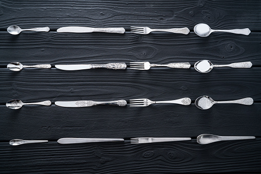 Cutlery home inventory in a row on black wooden background with fork spoon table knife and teaspoon