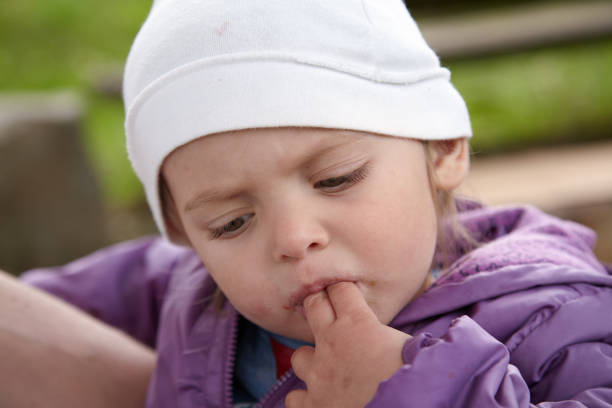 Portrait of a pensive little girl sucking two fingers in the backyard