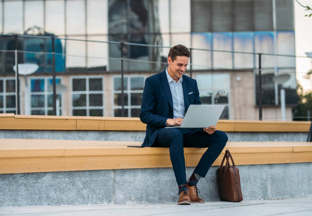 business on the go: uomo d'affari che lavora sul suo laptop per strada - outdoors business computer laptop foto e immagini stock