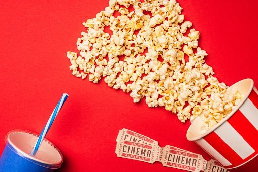 Top view of popcorn, cinema tickets and paper cup on red surface