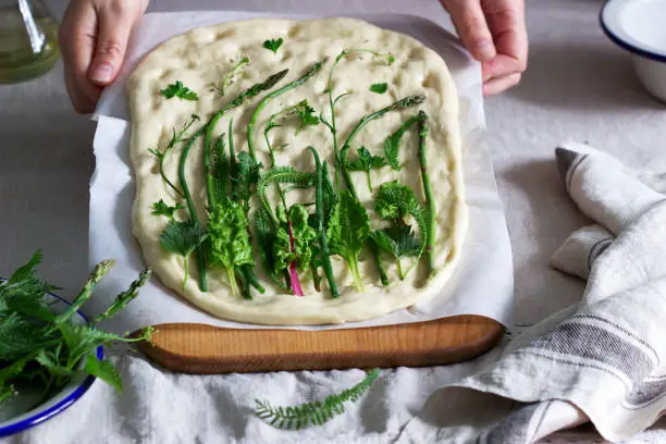 Woman makes focaccia from yeast dough with various herbs. Rustic style, selective focus.