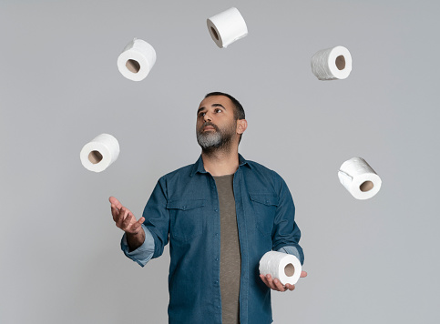 Man juggling with toilet papers over gray background
