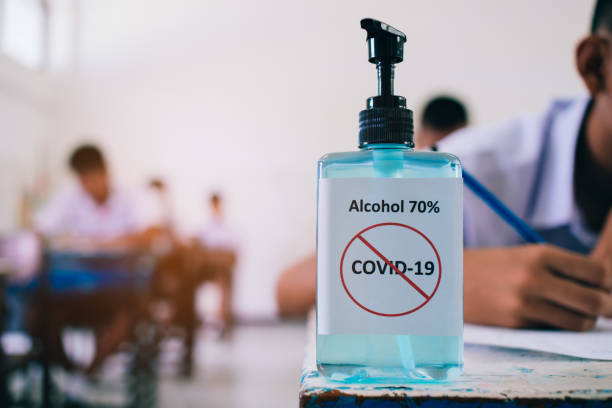 Alcohol 70%  Sanitizer standing for protect corona virus or covid-19 with students doing exam answer sheets exercises in classroom of school with stress. stock photo